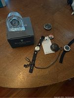 Overview photo showing two wristwatches, two pocket watches (one damaged), and Waterford crystal clock on table with box