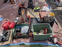 Photo showing wide variety of tools and containers spread on tarp including gas containers and hand saw