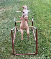 Front view of vintage horse ride-on toy showing horse head, standing on rust-colored metal frame with wooden handle grips