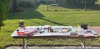 Full view of assorted household items laid out on table outdoors in sunlight