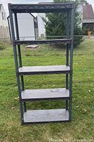 Full front view of black plastic shelving unit standing on grass outdoors, showing all 5 shelves and vertical supports.