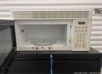Hotpoint white microwave oven with door open showing glass turntable inside and keypad on right side.