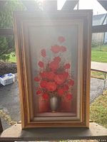 Full front view of the framed oil painting showing the bouquet of red flowers in a vase outdoors in natural light.