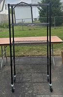 Full front view of the black metal wire shelving rack showing all four shelves and castor wheels.