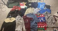 Wide view of multiple shirts including striped, solid, and logo T-shirts, hats, belts, and a sports bag laid flat on carpet.