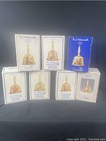 Photo of seven M.J. Hummel bell boxes grouped together showing printed editions and Goebel branding.