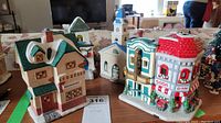 Front view of four ceramic miniature Christmas buildings on a wooden surface showing restaurant, soda shop, church, and house
