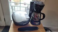 Black & Decker drip coffee maker and Lean Mean Fat Grilling Machine grill side by side on a small table.