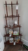 Full view of the five-shelf dark wood corner display unit with decorative turned supports, shelves arranged in a triangle shape. Several decorative items are displayed on the shelves but are not included in the lot.