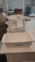 Three Corningware casserole dishes with lids and a rectangular loaf dish on a countertop, featuring the blue cornflower pattern.