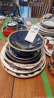 Stack of various decorative plates with a large blue serving bowl on top, showing overall composition of the lot