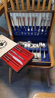 Overall view of Wm Rogers silverplate flatware set with spoons, forks, and knives displayed in wooden case, also showing Gourmet Tableware steak knives in red box.