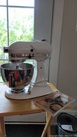 Front view of white mixer assembled on table with stainless bowl and instruction booklet