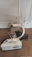 White Oreck XL portable vacuum cleaner with hose, carry strap, and user manual. Included vacuum bags and plastic extension tubes are grouped behind the vacuum on a wooden floor.