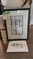 Framed and matted line drawing with signature, showing vertical image of wooden cabin and trees.