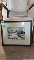Framed and matted oil painting of a harbour scene resting on a chair, showing the entire piece and frame.