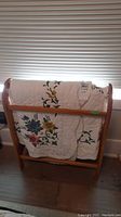 Wooden quilt rack with quilt draped over it.