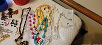 Overview of various 1980s style colorful bead necklaces alongside other jewelry pieces laid on a surface.