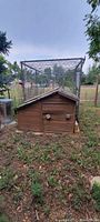 Front photo of the wooden duck coop and attached chain-link enclosure, showing small doors and coop design