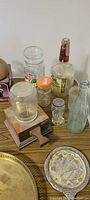Various glass bottles including clear jars, liquor bottle, salt shaker, and a green tinted bottle, placed on wooden cutting boards and an old wooden base.