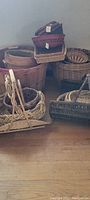 Photo of multiple baskets stacked and arranged on floor against wall, showing sizes, shapes, and handles.