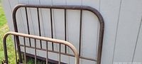 Metal and wooden bed frames placed outdoors against a wall, showing headboards and footboards with wear and rust.