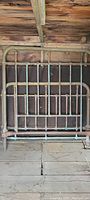 Old brass bed frame leaning against a wooden wall showing rust and weathering on a wooden floor.