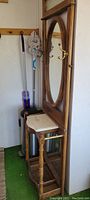 Full view of wooden coat rack with oval mirror and marble shelf, alongside broom and trash can