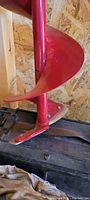 Close-up photo of the red spiral blade of the soil auger showing blade details and mounting bracket.