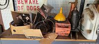 Shelf with yellow funnel, red metal oil canister, assorted wires or belts, manuals in box, and white container