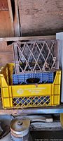 Three stacked plastic milk crates in yellow, blue, and black with diamond ventilation pattern