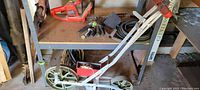 Manual push garden plow with wheels and handle, shown in front of garage shelf