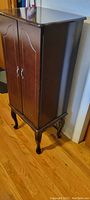 Jewelry armoire at three-quarter angle showing wood finish and cabriole legs
