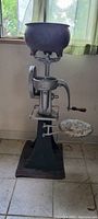 Front angle view of the milk separator showing the large upper bowl, crank handle, and base with rust and wear.