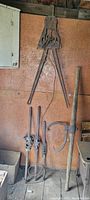 Wide shot showing all tools hanging or leaning on a wall in a shed, including pipe threaders and large handle tools