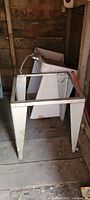 Photo of large metal stand painted white with visible wear, rust and some wood panel background