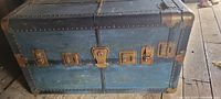 Front view of blue steamer trunk with metal hardware and visible damage on right side edge