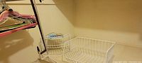 White wire storage baskets, hanging closet rod with hangers including pink and black plastic hangers, shown hanging on closet rod.