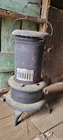 Photo of first vintage portable kerosene stove with embossed cast iron door and perforated metal body taken indoors on wooden floor