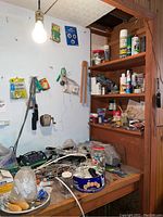 Workbench with electrical cords, light bulbs, small lamp with etched glass shade, wire connectors, and various small hardware items on and hanging around the workbench