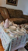 Wide view of cream and sugar set, plates, teapot, and gravy boats on floral tablecloth in living room