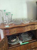 Photo showing a large glass serving tray and various divided dishes on and inside a wooden cabinet.