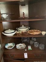 Full view of shelves with assorted glass and china serving dishes, plates, and tumblers.