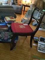 Side view of carved wood dining chair with red needlepoint floral seat in living room setting