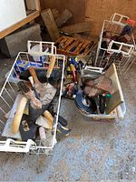 Basket containing various hand tools including brushes, trowels, measuring tapes, screwdrivers, sanding tools, pry bars, rubber mallet, level, chisels, clamps in a garage setting.