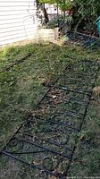 Four iron fence panels lying on grass with black decorative scrollwork, some corrosion and weathering visible.