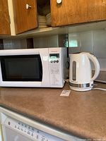 Photo showing Panasonic microwave next to Hamilton Beach electric kettle on kitchen counter.
