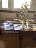 View of entire table showing two extra small landscape oil paintings on small wooden easel, collection of postcards spread flat, Easter tree with decorated eggs, and thimbles.