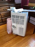 Full view of TCL portable air conditioner on wheels with hose and remote on top; unit in white color