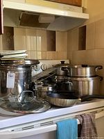 Photo of various pots and pans on stovetop and counter, showing large stock pot, Dutch ovens, smaller pots with lids, and fry pan.